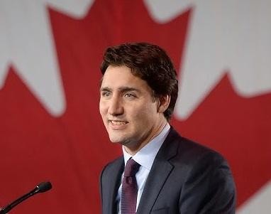 Justin Trudeau rozmawiający z grupą Kanadyjczyków na świeżym powietrzu, uśmiechnięty i zaangażowany.