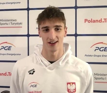 Ksawery Masiuk uśmiecha się, z basenem lub medalem w tle, emanując inspiracją i determinacją.