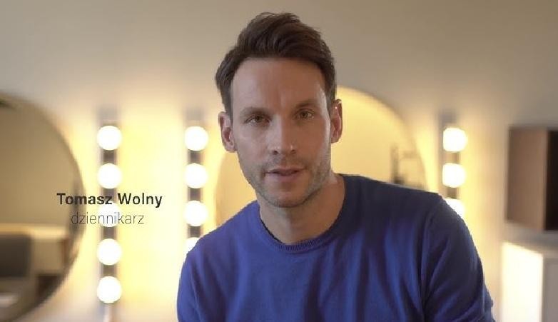 Tomasz Wolny na planie telewizyjnym, w dynamicznej pozie prezentera, z tłem sugerującym studio informacyjne, symbolizujący jego karierę medialną i zaangażowanie w pracę.