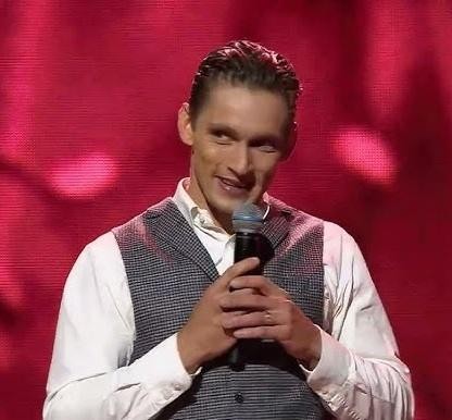 Filip Gurłacz w naturalnej pozie, ukazujący refleksyjny wyraz twarzy, w swobodnym otoczeniu.