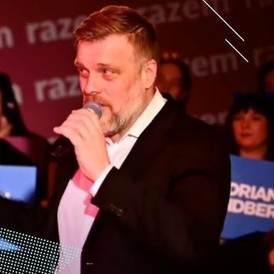 Adrian Zandberg podczas spotkania publicznego, rozmawiający z wyborcami, ukazujący jego zaangażowanie i bliskość z ludźmi.