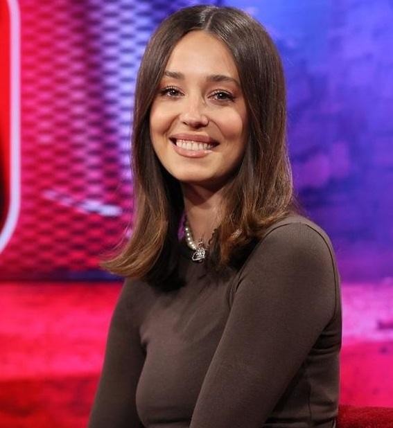 Izabella Krzan uśmiechnięta w swoim nowoczesnym mieszkaniu z roślinami doniczkowymi, ukazująca ciepło i naturalność.
