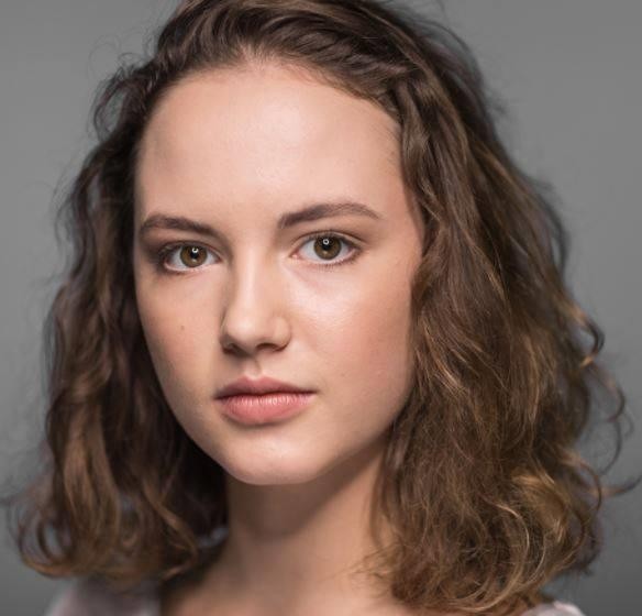 Martyna Byczkowska na planie filmowym, w stroju nawiązującym do jednej z jej ról, z naturalnym uśmiechem i subtelnie widocznym sprzętem filmowym w tle.