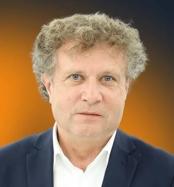 Jacek Karnowski podczas uprawiania żeglarstwa, na jachcie, z pełnymi żaglami i malowniczym tłem wybrzeża.